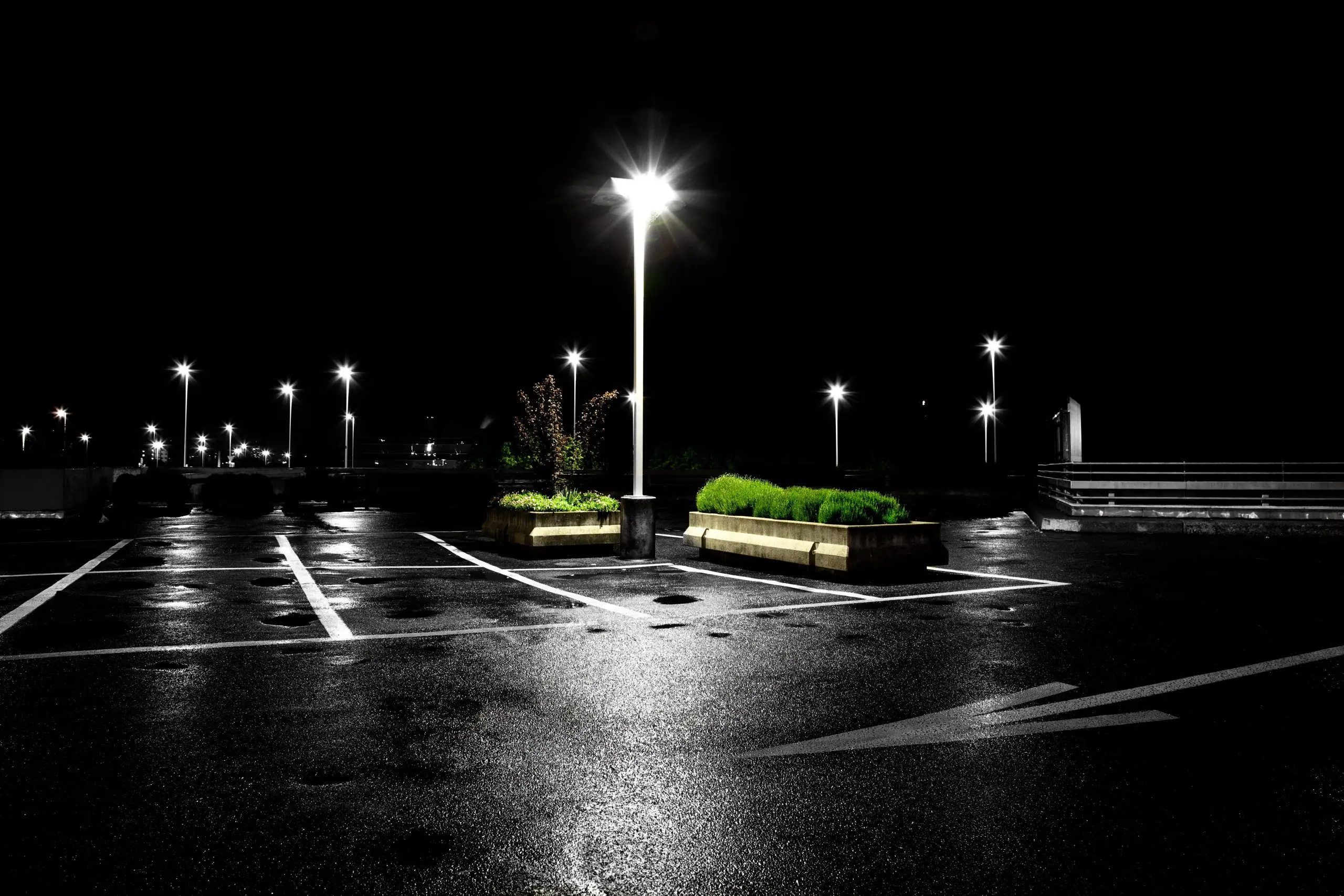 Nighttime parking lot with LED pole lighting illuminating wet pavement and landscaped planters