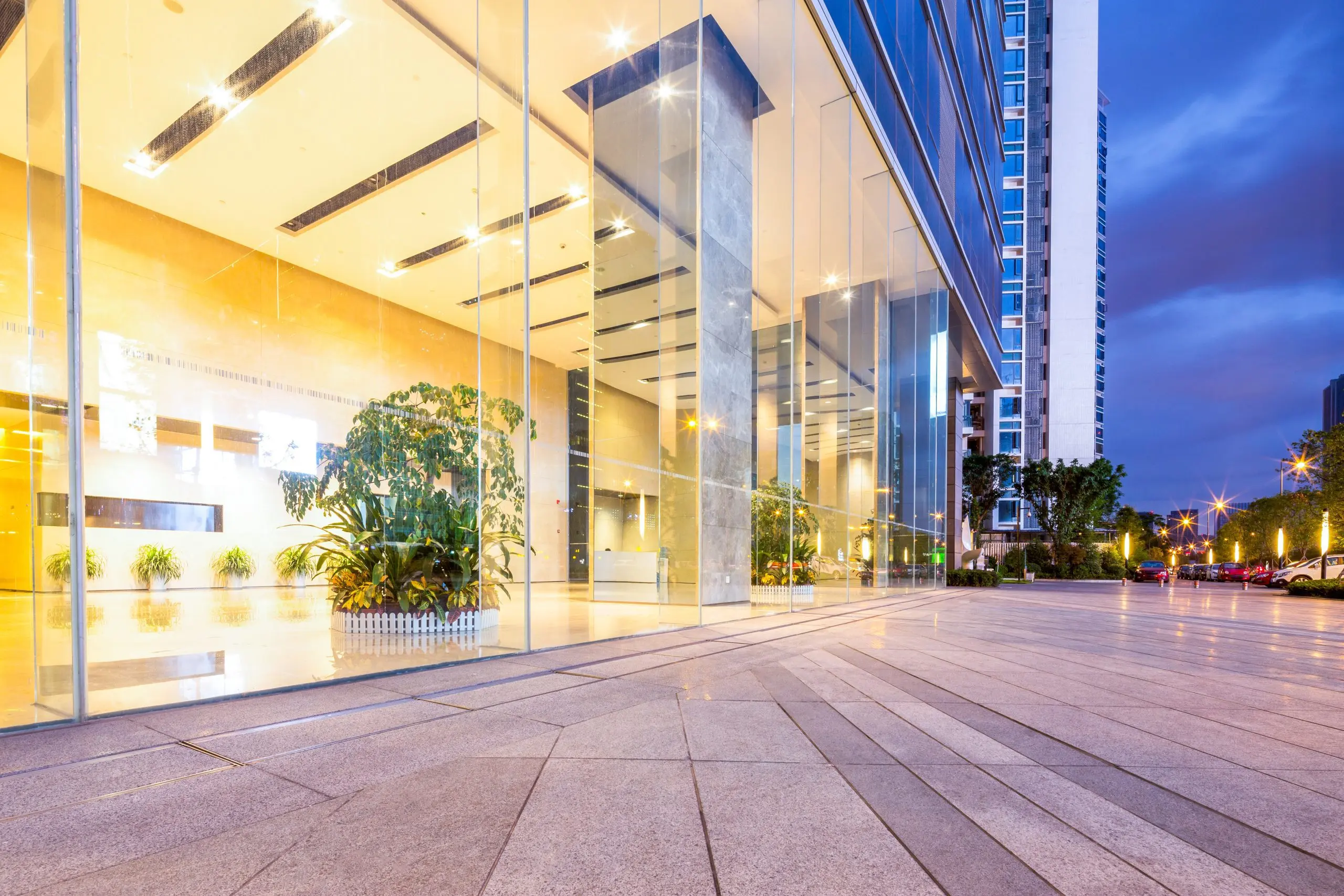 Modern commercial building entrance illuminated at dusk with glass storefront and landscaping