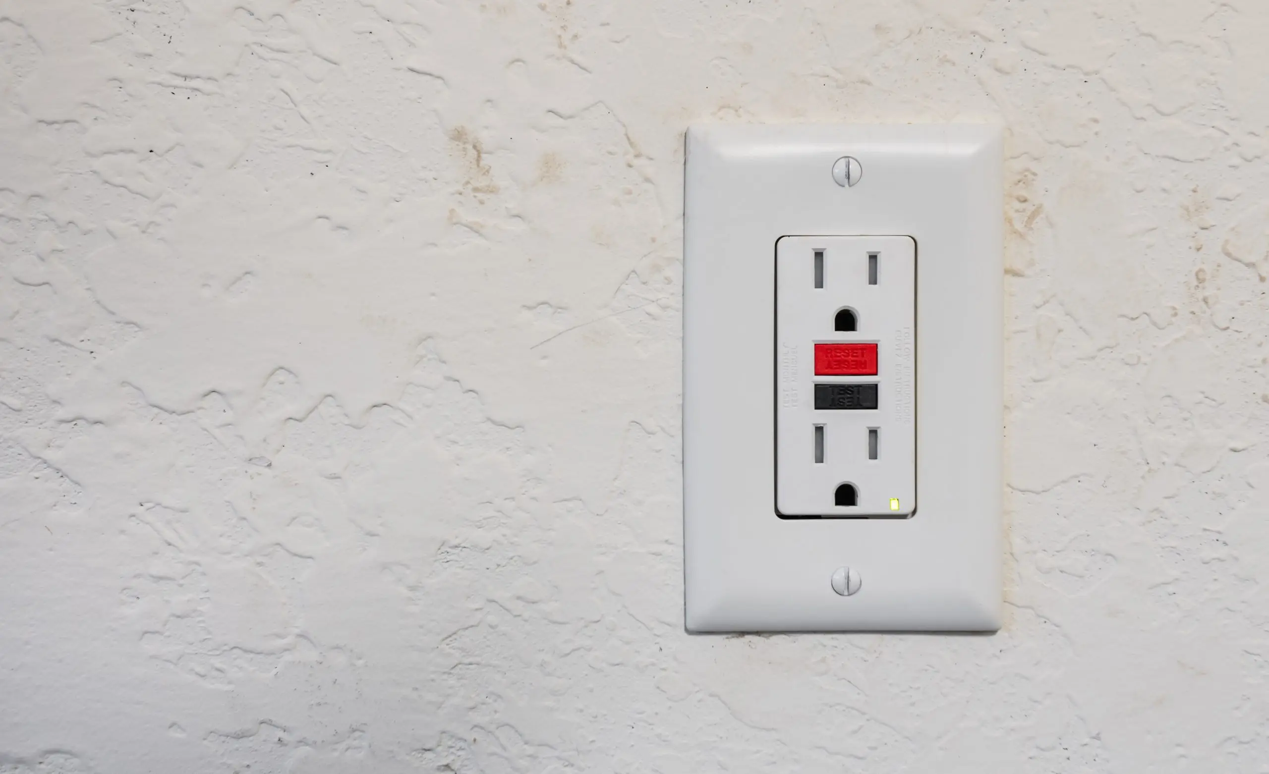 White electrical outlet with red and black GFCI buttons on textured wall