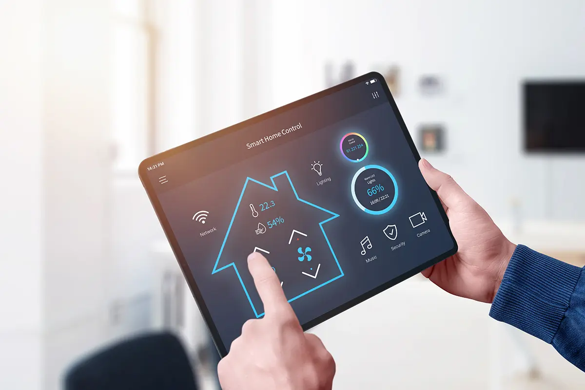 Hand holding tablet displaying smart home control interface with icons for lighting, temperature, and security