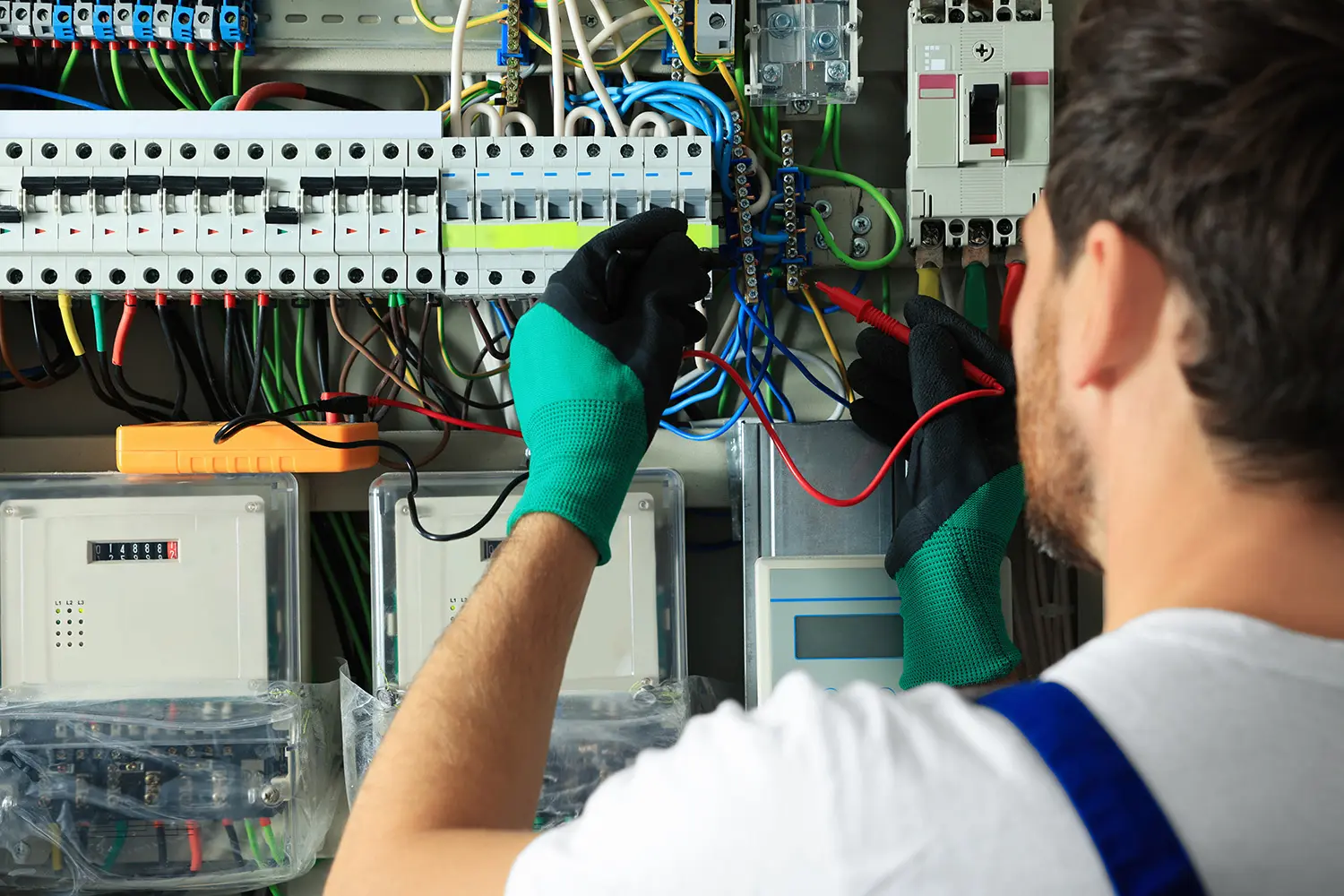 Electrician in green gloves working on circuit breaker panel with wires