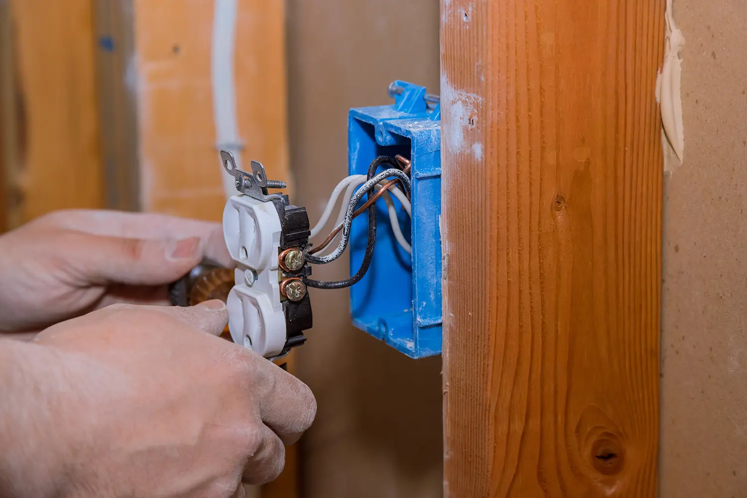 Electrician installing white outlet with blue wire box on wooden wall