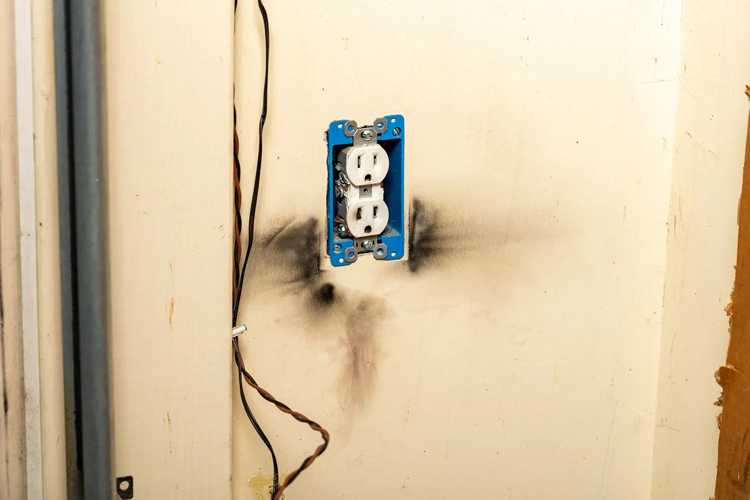 Damaged wall with scorched marks around blue electrical outlet box